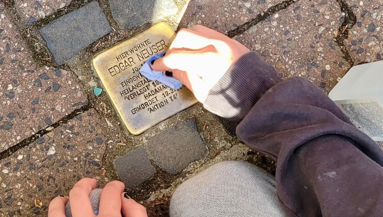 Kinderhand beim Reinigen eines Stolpersteins