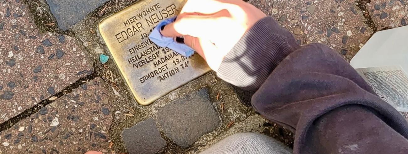 Kinderhand beim Reinigen eines Stolpersteins
