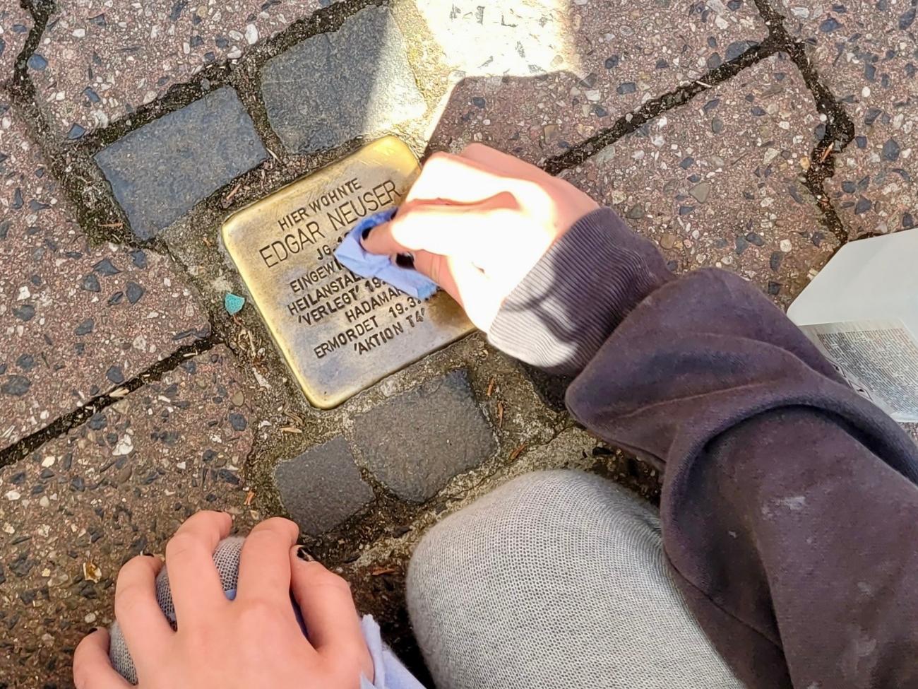 Kinderhand beim Reinigen eines Stolpersteins